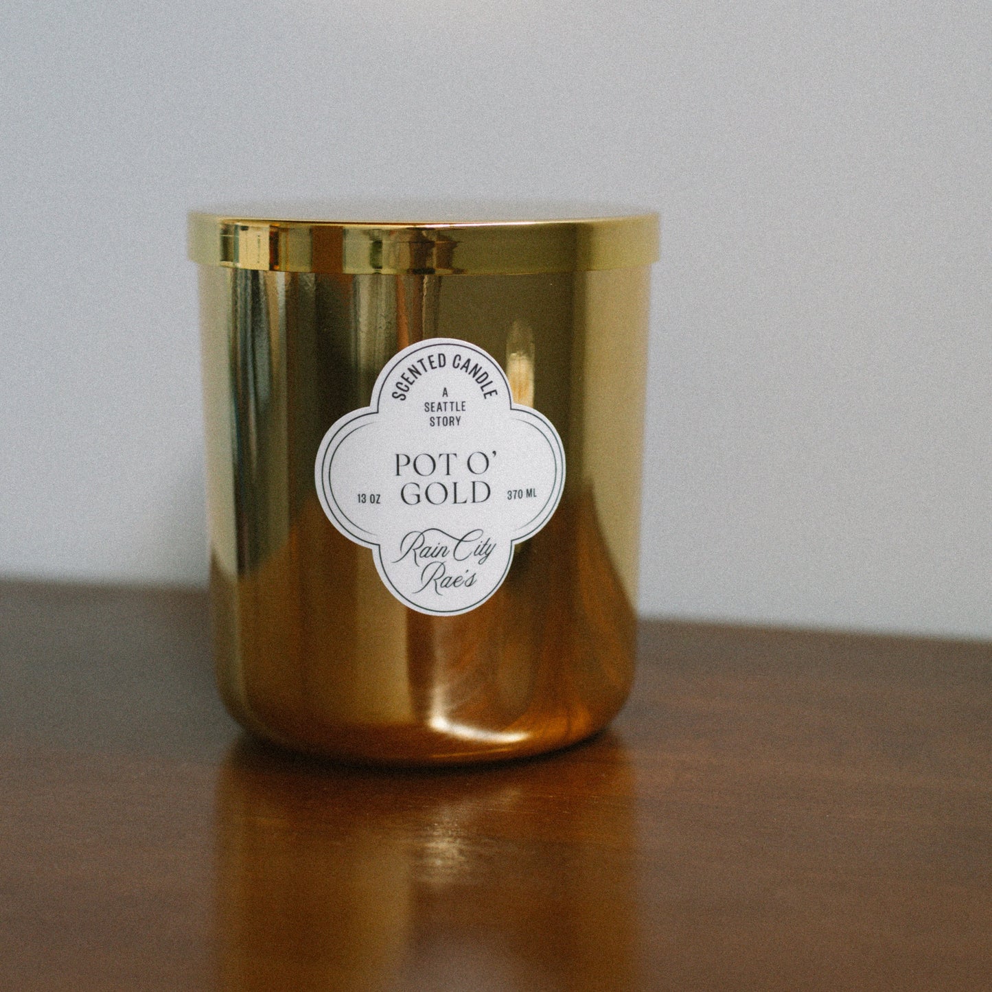Gold candle with a flower bespoke label on a wooden surface and light gray background
