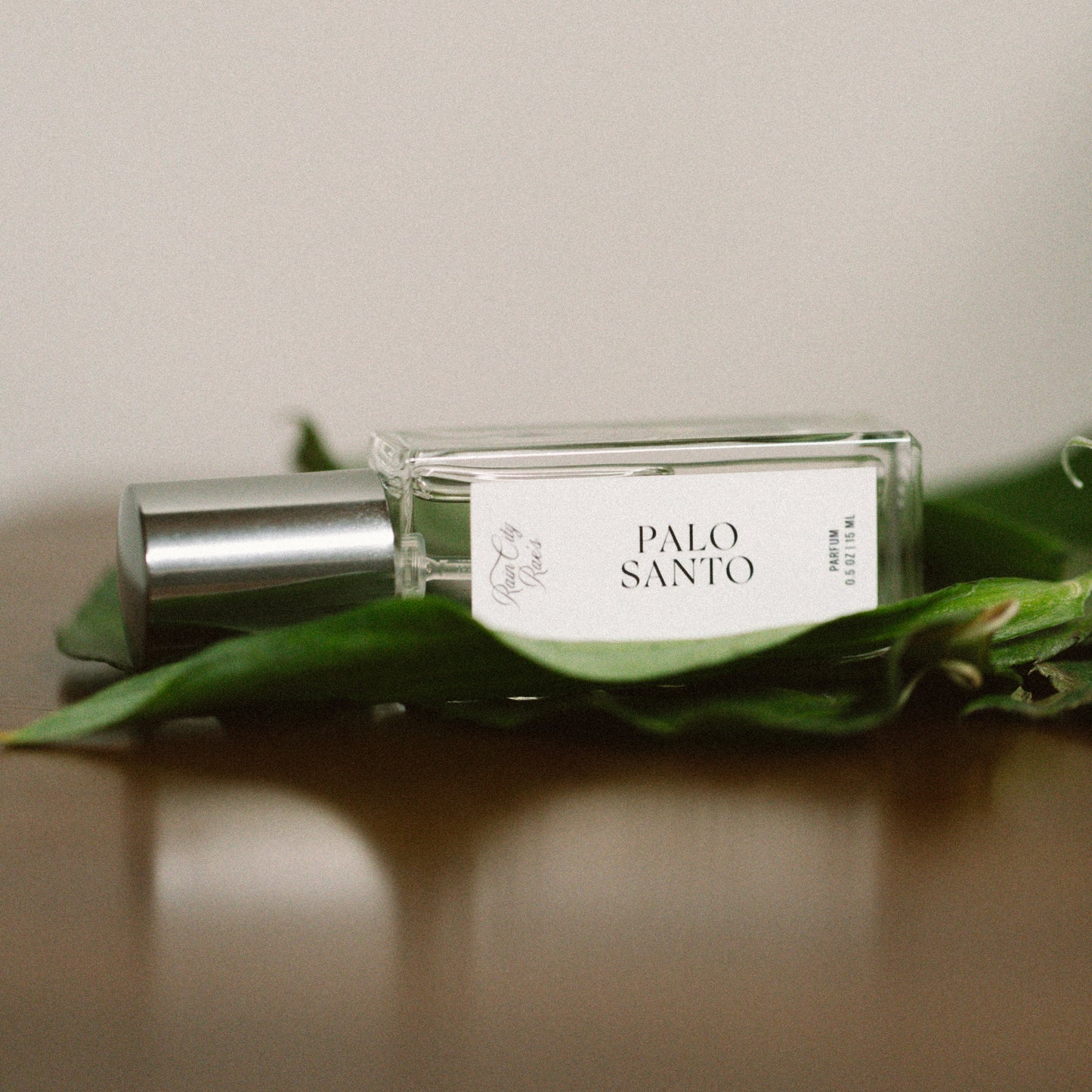 Perfume bottle labeled 'Palo Santo' on green leaves with a neutral background