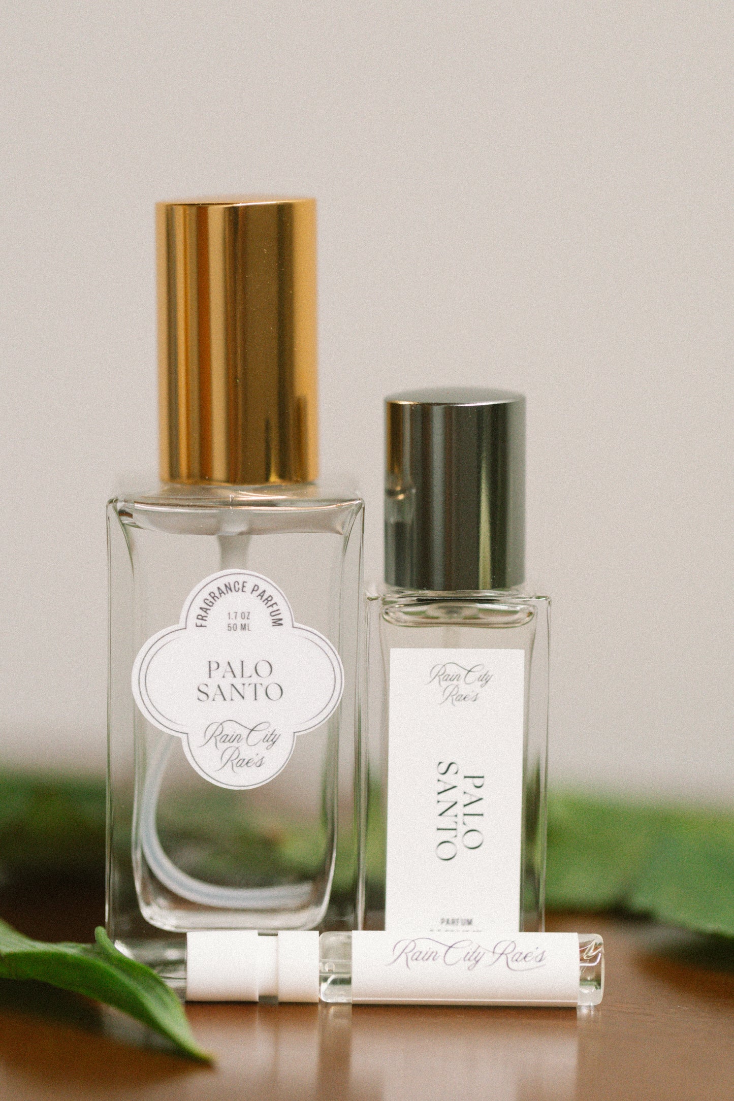 Two Palo Santo perfume bottles on a wooden surface with green leaves in the background.