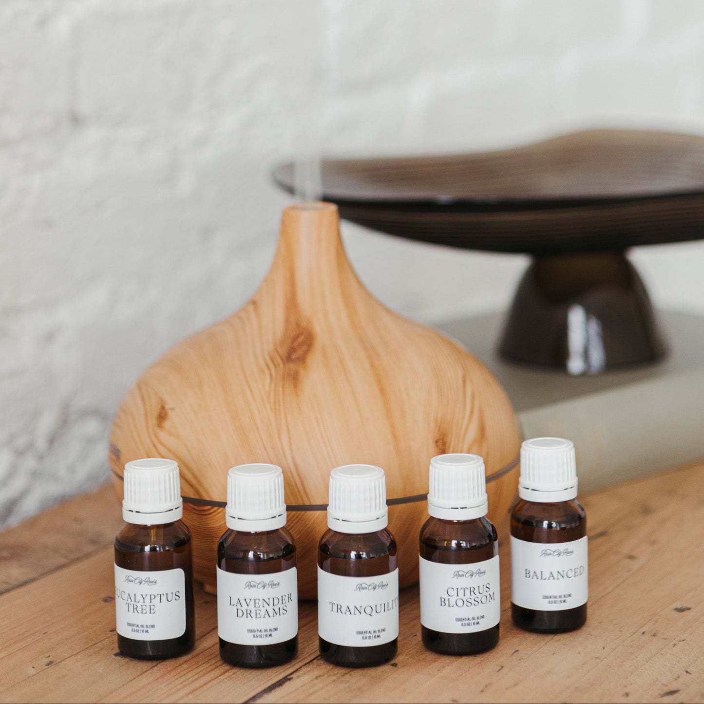 Five small bottles of essential oils on a wooden surface with a textured white wall in the background.